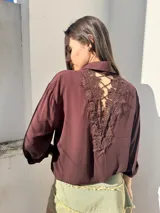 Camisa color borgoña con cuello clásico, cierre frontal con botones, bolsillo de parche con encaje en el pecho y mangas largas con lazo en los puños.