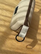 Neceser color beige de forma rectangular, con cierre superior y asa de mano.