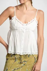 Blusa blanca de algodón con tirantes finos y escote en V. Presenta detalles de encaje en el escote y en el ruedo, y cierre frontal con botones.