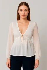 Blusa color marfil con escote en V, mangas largas abullonadas y detalle de lazo en el centro del busto.