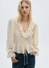 Blusa color crema con estampado de lunares, escote en V con volantes y lazos, mangas largas abullonadas con puños elásticos y corte peplum.