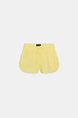 Shorts de tiro bajo color amarillo claro, confeccionado en tejido con lino. Presenta cintura elástica ajustable con cordones y aberturas laterales en el bajo.