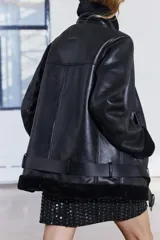 Cazadora negra de Zara Woman Collection, con cuello solapa y manga larga. Tiene bolsillos con cremallera en el delantero, interior de borreguillo combinado a tono y bajo con cinturón ajustable con hebilla metálica. El cierre es frontal con cremallera.