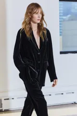 Pantalón de terciopelo negro de tiro medio, con bolsillos delanteros y traseros, pierna recta y cierre frontal con cremallera, botón y gancho metálico.