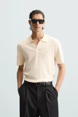 Polo color crema de punto, corte regular fit, con cuello solapa y abertura frontal.