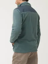 Campera polar RKF modelo Volterra color verde grisáceo, con cierre frontal completo, cuello alto y mangas largas. Presenta aplicaciones de tela canvas de algodón en los hombros, dos bolsillos frontales con cierre y bolsillos internos. Confeccionada en poliéster reciclado.