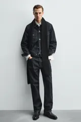 Botín de cuero negro con punta cuadrada, caña corta y cierre lateral con cremallera. Presenta una correa con hebilla metálica alrededor del tobillo.