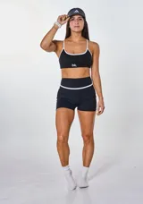 Conjunto deportivo negro con detalles en blanco, compuesto por un top con breteles finos y un short ajustado.