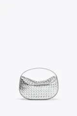 Bolso de mano plateado con efecto trenzado y asa corta. Incluye correa extraíble para usar como bandolera. Cierre con cremallera metálica.