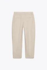 Pantalón color beige de tiro medio con cintura elástica ajustable con cordones, bolsillos delanteros y falsos bolsillos de vivo en la espalda. El bajo es ajustable con botón a presión.