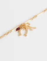 Collar dorado con cadena de eslabones grandes y dijes colgantes de corazón rojo, herradura y moño con strass.