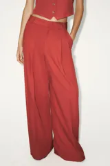 Pantalón color ladrillo de corte palazzo, con bolsillos laterales y traseros, detalle de pliegues en el frente y cierre frontal con cremallera, botón interior y gancho metálico. Confeccionado en hilatura con 21% de lino.