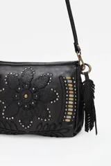 Cartera de cuero negro con diseño de flor mandala en relieve y apliques de tachas doradas y plateadas. Presenta flecos colgantes en uno de los laterales y correa ajustable para llevar al hombro o cruzada.