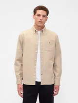 Camisa de manga larga color beige, de corte clásico, con cuello abotonado, bolsillo en el pecho y logo de oso bordado.
