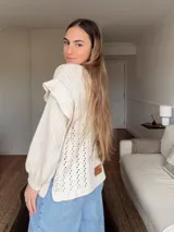 Sweater de punto calado color crema, con mangas largas y volados en los hombros. Tiene corte holgado y etiqueta de cuero con logo en la parte inferior.