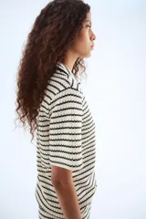 Top de punto con textura a rayas horizontales en blanco y negro. Tiene cuello camisero abierto, mangas cortas y corte holgado.