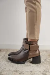 Bota corta de cuero marrón con puntera redondeada y taco cuadrado. Presenta una correa con hebilla alrededor del tobillo y cierre lateral.