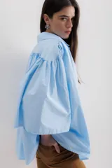 Camisa celeste de algodón con corte amplio, cuello camisero y mangas largas con puños abullonados.