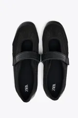 Zapato tipo bailarina color negro, con capellada de rejilla y cierre con tira de velcro.