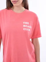 Remera color salmón con estampado frontal con la frase "The Beach Club" en letras blancas.