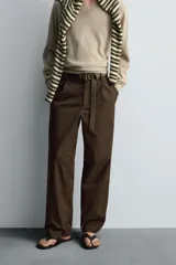 Pantalón relaxed fit color marrón confeccionado en tejido de algodón con estructura twill. Cintura con pliegues frontales, bolsillos laterales en cadera y detalle de bolsillos traseros de doble vivo con botón. Cierre frontal con cremallera y botón.