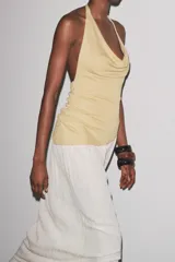 Vestido largo de fiesta con cuello halter fluido y hombros descubiertos. Presenta un top dorado drapeado y una falda larga color crema con textura.