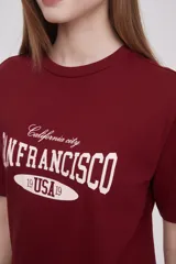 Remera color borgoña de corte holgado, con cuello redondo y mangas cortas. Estampado frontal con el texto "California city San Francisco 19 USA 19" en color blanco.