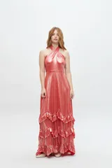 Vestido largo color salmón metalizado con escote halter cruzado y espalda descubierta. Falda larga con volados en capas.