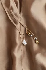 Blusa color dorado de lyocell con cuello redondo con cordón ajustable, abertura en V y mangas globo largas con puños vueltos con abertura y botón.
