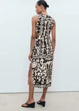 Vestido midi sin mangas, con cuello redondo y diseño recto. Presenta un estampado de estilo batik o animal print en tonos blanco roto y marrón oscuro, con aberturas tipo cut-out en los laterales de la cintura y una abertura lateral en el bajo.