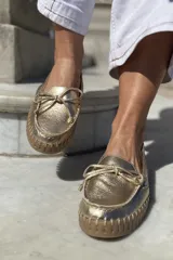 Mocasín náutico dorado de cuero con detalle de lazo en la parte delantera y suela de goma color caramelo.
