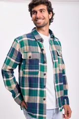 Camisa de franela a cuadros en tonos verde, azul marino, beige y gris. Tiene cuello clásico, cierre con botones, dos bolsillos con botón en el pecho y corte recto.