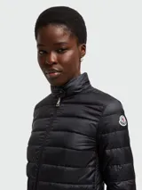 Chaqueta acolchada (tipo puffer) de color negro, con cuello alto y cierre frontal de cremallera. Presenta dos bolsillos frontales con solapa y cierre a presión.