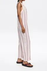 Mono largo de lino color crudo con rayas verticales rojas y azules. Tiene corte recto, escote redondeado pronunciado, tirantes anchos con trabillas para fruncir y espalda nadadora.