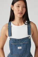 Jardinero corto de jean azul con tirantes ajustables, bolsillo en el pecho y botones metálicos a los lados.