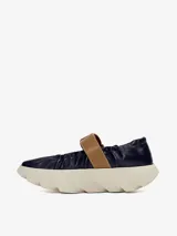 Zapato de cuero azul marino con correa marrón con hebilla dorada y suela de goma blanca con diseño ondulado.