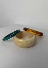 Set de tres pulseras rígidas de diferentes colores y materiales: una verde lisa, una beige con efecto marmolado y una color ámbar facetada.