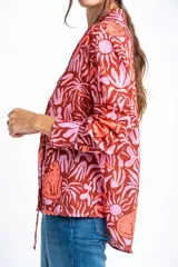 Blusa oversize de poliéster con estampado de animales y plantas en tonos rosa y marrón. Tiene cuello camisero, mangas largas y cierre frontal con lazos.