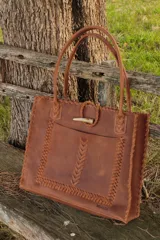 Bolso tote de cuero color marrón con costuras decorativas y cierre con presilla de asta. Tiene doble asa de mano y bolsillo externo con costuras decorativas.