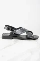 Sandalias bajas negras de cuero charol con tiras cruzadas y tachas plateadas.