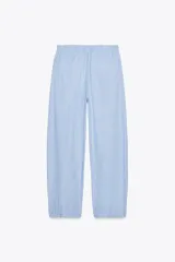 Pantalón tipo barrel con rayas verticales celestes y blancas, tiro medio y cintura elástica ajustable con lazo. Tiene bolsillos laterales y falsos bolsillos de vivo en la espalda.