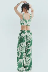 Pantalón ancho de punto con estampado floral blanco sobre fondo verde. Tiene tiro alto, cintura elástica y piernas amplias.