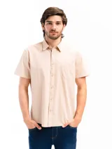 Camisa de manga corta color beige, confeccionada en 100% algodón, con cuello clásico, cierre frontal con botones y bolsillo en el pecho.