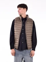 Chaleco acolchado color beige con cierre frontal y cuello alto. Diseño sin mangas con bolsillos laterales. Ideal para usar sobre camisas o sweaters.
