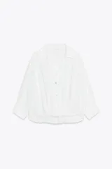 Camisa blanca de cuello solapa y manga larga con puños. Tiene un nudo en la parte delantera y cierre frontal con botones.