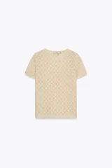Top color crema de tejido de punto calado con patrón de rombos, cuello redondo, manga corta y cierre frontal con ganchos metálicos.