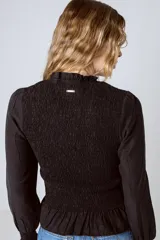 Blusa negra con cuello alto fruncido, mangas largas abullonadas y detalle de volado en el ruedo.