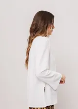 Camisa blanca de cuello redondo con frunces, abotonada y de manga larga con puño abierto.
