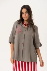 Camisa verde de silueta oversize con cuello camisero y manga 3/4. Tiene bordados de coral y caracol en el frente y botones a tono.