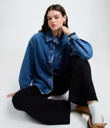 Camisa oversized de jean azul, con cuello padre, mangas largas con puños abotonados y cierre frontal con botones. Incluye un bolsillo aplicado en el pecho y bajo redondeado.